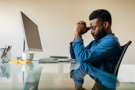 Upset pensive black businessman sitting at desk with computer, male professional analyst thinking of problem solutionの写真素材