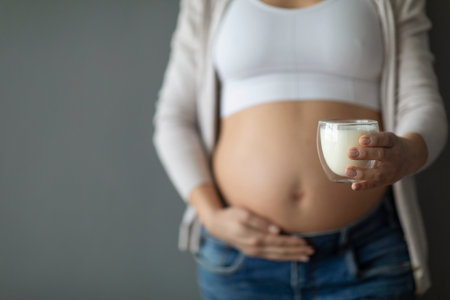 Pregnant Woman Holding Glass Of Milk And Caressing Belly Over Grey Backgroundの写真素材