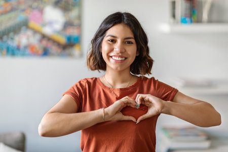 Smiling Young Arab Woman Showing Heart Gesture With Hands Near Chestの写真素材