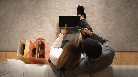 Young arab man hug european wife, ordering purchase on computer with blank screen, enjoy online shoppingの写真素材