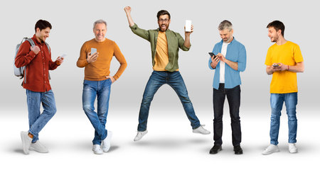 Cheerful emotional young and adult men in casual jumping, typing on smartphone with empty screen