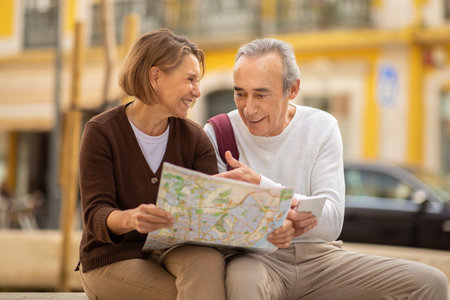 Happy Senior Couple Holding Travel Map Sitting Outdoorsの写真素材