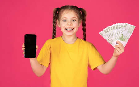 Happy Little Girl Showing Blank Smartphone And Euro Cash Money At Cameraの写真素材