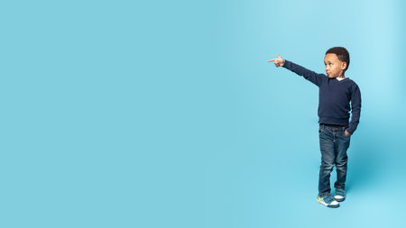 Cool offer. Happy african american adorable boy pointing aside at free space, standing on blue background, panoramaの写真素材