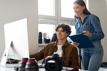 Young male photographer and his assistant looking at photographs on computer, selecting photos togetherの写真素材