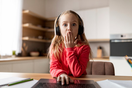 Omg. Pov shot of shocked schoolgirl in headphones using laptop at homeの写真素材