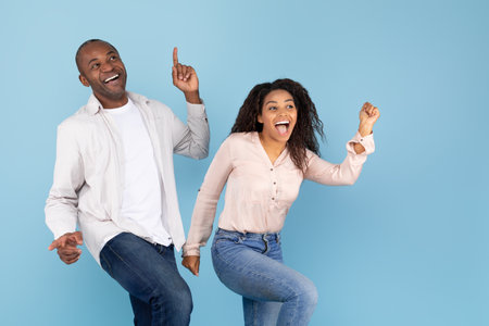 Overjoyed black middle aged man and young woman having fun together and dancing on blue background, copy spaceの写真素材