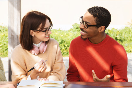 Happy young african american man and european female students study with book together, talkの写真素材