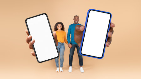 Discount app. Happy black couple showing big smartphones with blank white screens at camera, mockup,...