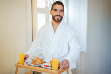 Man Holding Table Tray With Breakfast Standing In Hotel Roomの写真素材