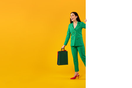 Happy stylish lady with shopping bags peeking from blank white banner with space for ad on yellow background, free spaceの写真素材
