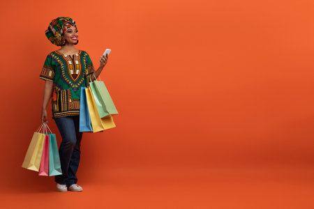 Happy african woman shopping online, using smartphone on orangeの写真素材