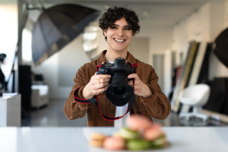 Young male food photographer using digital camera and taking photo of dessert, looking and smiling at cameraの写真素材