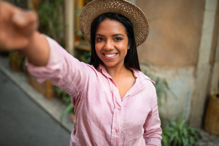 Smiling millennial african american woman tourist in hat taking selfie on smartphone enjoy travel in city, outdoorの写真素材