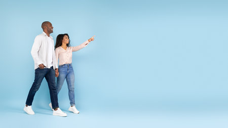 Excited african american spouses holding hands and walking, pointing and looking at copy space for ad, bannerの写真素材