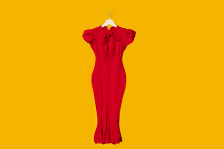 Bright beautiful classic elegant red dress on wooden hangers isolated on yellow studio background, free spaceの写真素材