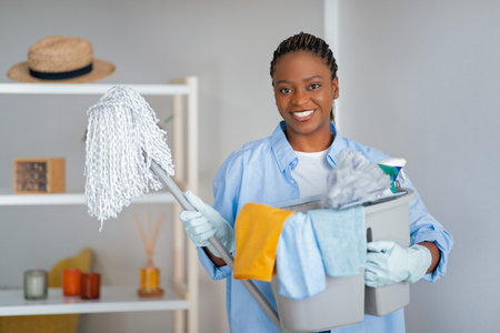 Cheerful pretty young black woman holding cleaning toolsの写真素材