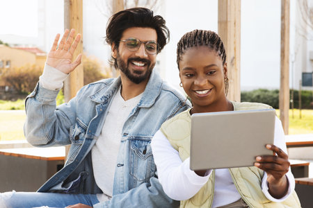 Smiling young black and arabic people students studying with tablet together, have meeting, waving...