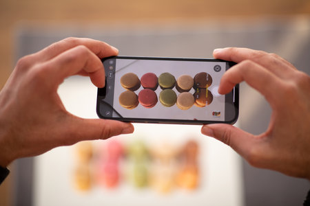 Male hands holding smartphone with broken screen, taking macarons photo
