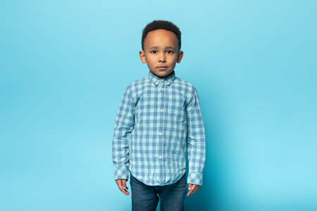 Portrait of adorable black boy in casual outfit posing over blue background and looking at camera, free spaceの写真素材