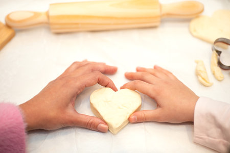 Hands of european little girl and adult mother make heart shaped cookies from dough with flour and rolling pinの写真素材
