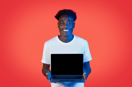 Positive black man showing laptop with blank screen on redの写真素材