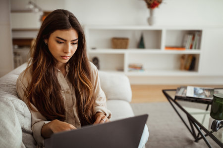 Busy serious millennial mixed race lady typing on laptop in living room interior, close upの写真素材