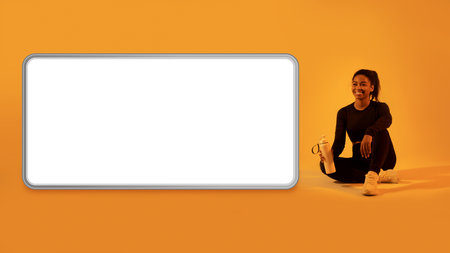 Workout app. Black lady sitting near huge cellphone screen, resting after training on orange neon...