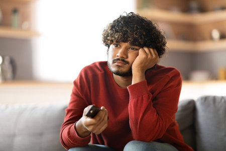 Boring Program. Portrait Of Upset Young Indian Man Watching TV At Homeの写真素材