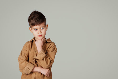 Pensive little european boy thinks, looks at empty space, isolated on gray studio backgroundの写真素材