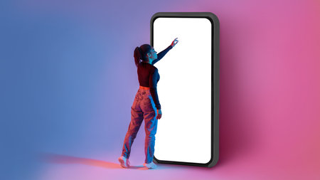 Full length shot of black lady touching screen of huge smartphone in neon light, mockup for app or...