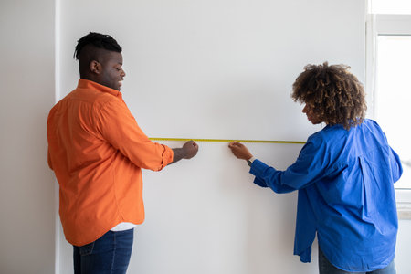Black Couple Measuring Wall With Tape Ruler While Making Repairing At Homeの写真素材