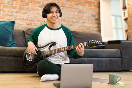 Japanese Guy Playing Electric Guitar Wearing Earphones Near Laptop Indoorの写真素材