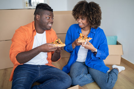 Young Black Couple Eating Pizza And Relaxing On Floor On Moving Dayの写真素材