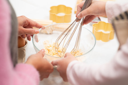Hands of european lady and little girl in aprons preparing cookie dough in kitchen, croppedの写真素材