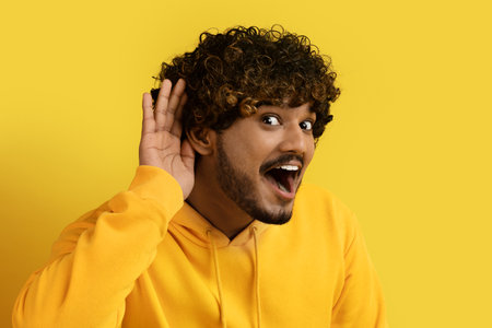 Excited indian guy holding hand next to earの写真素材