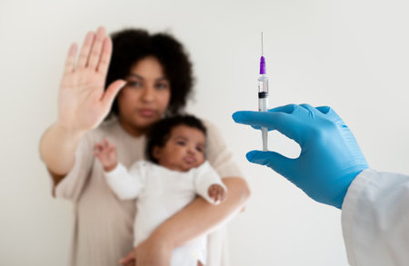 Serious loving young african american woman hold baby in arms, making stop gesture with hand from doctor with syringeの写真素材