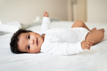 Cute little african american baby lies on bed, rest and relax, enjoy free time and good morning in white bedroomの写真素材