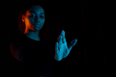 Virtual reality concept. Young african american lady stretching hand and touching invisible touchscreen, neon lightの写真素材