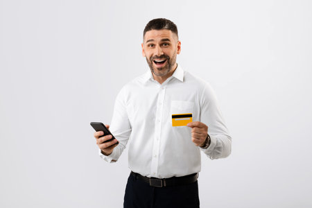 Excited businessman in shirt using smartphone and credit card for shopping online, paying for...