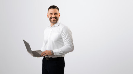 Happy successful middle aged businessman in white shirt working with laptop and looking aside at copy space, panoramaの写真素材