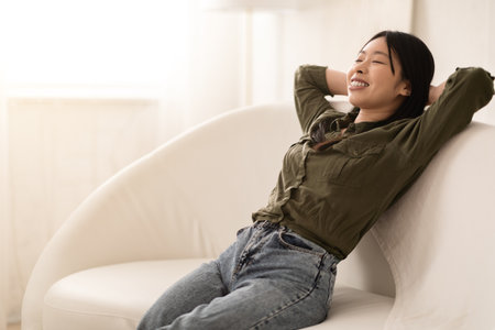 Beautiful young asian woman relaxing on couch in living roomの写真素材
