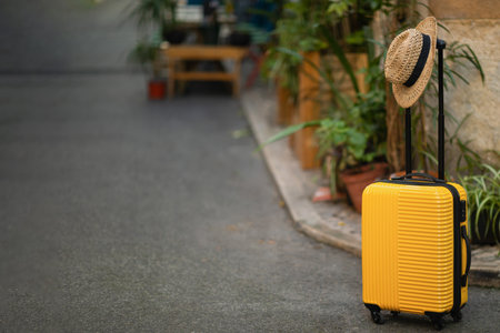 Yellow big suitcase with hat on street road with plants, accessories for trip for tourist free space, close upの写真素材