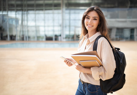 Happy young european woman student in casual with backpack, books and smartphone go to studyの写真素材