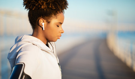 Young Black Female Wearing Wireless Earphones Standing With Closed Eyes Outdoorsの写真素材