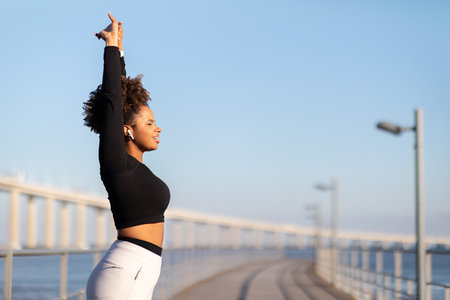Sporty black woman raising hands, stretching arm muscles while training outdoorsの写真素材