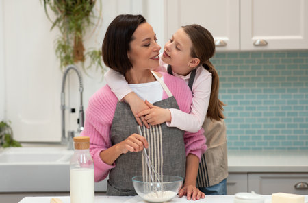 Cheerful caucasian little daughter hugs young mother in apron make dough for cookies have fun in kitchenの写真素材