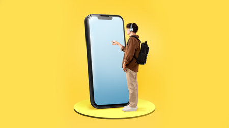 Male Student Using Large Smartphone With Blank Screen, Yellow Backgroundの写真素材