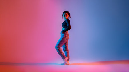 Full length of stylish african american woman posing in neon light in studio and smiling at cameraの写真素材