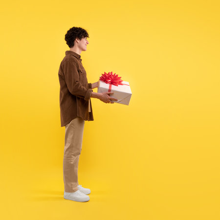 Side View Of Happy Man Holding Gift Box, Yellow Backgroundの写真素材